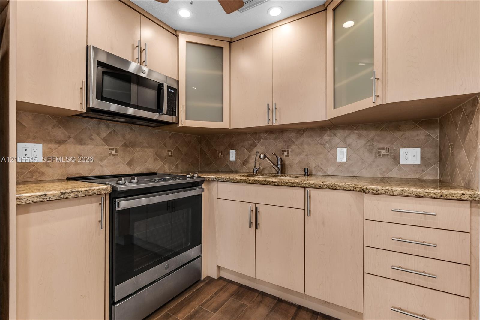 Kitchen featuring light wood-finish cabinetry, stainless steel appliances, granite countertops, and a tiled backsplash