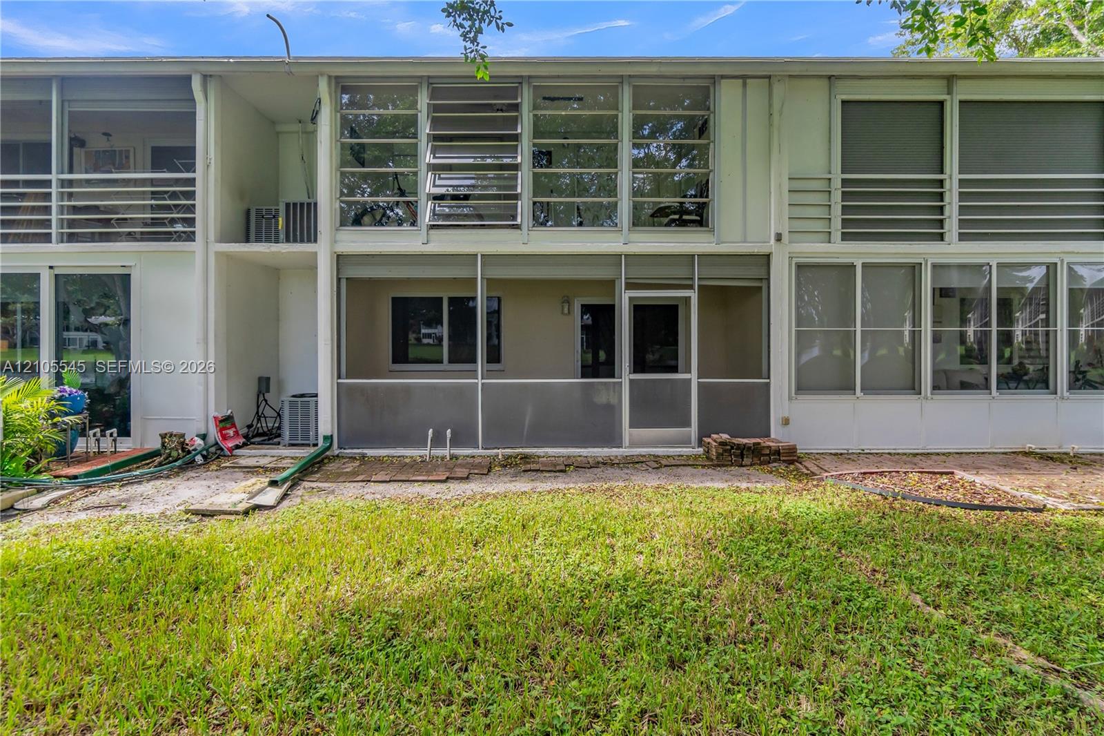 Screened patio with a white framed door, sliding glass doors, upper-level windows, and a grassy outdoor area