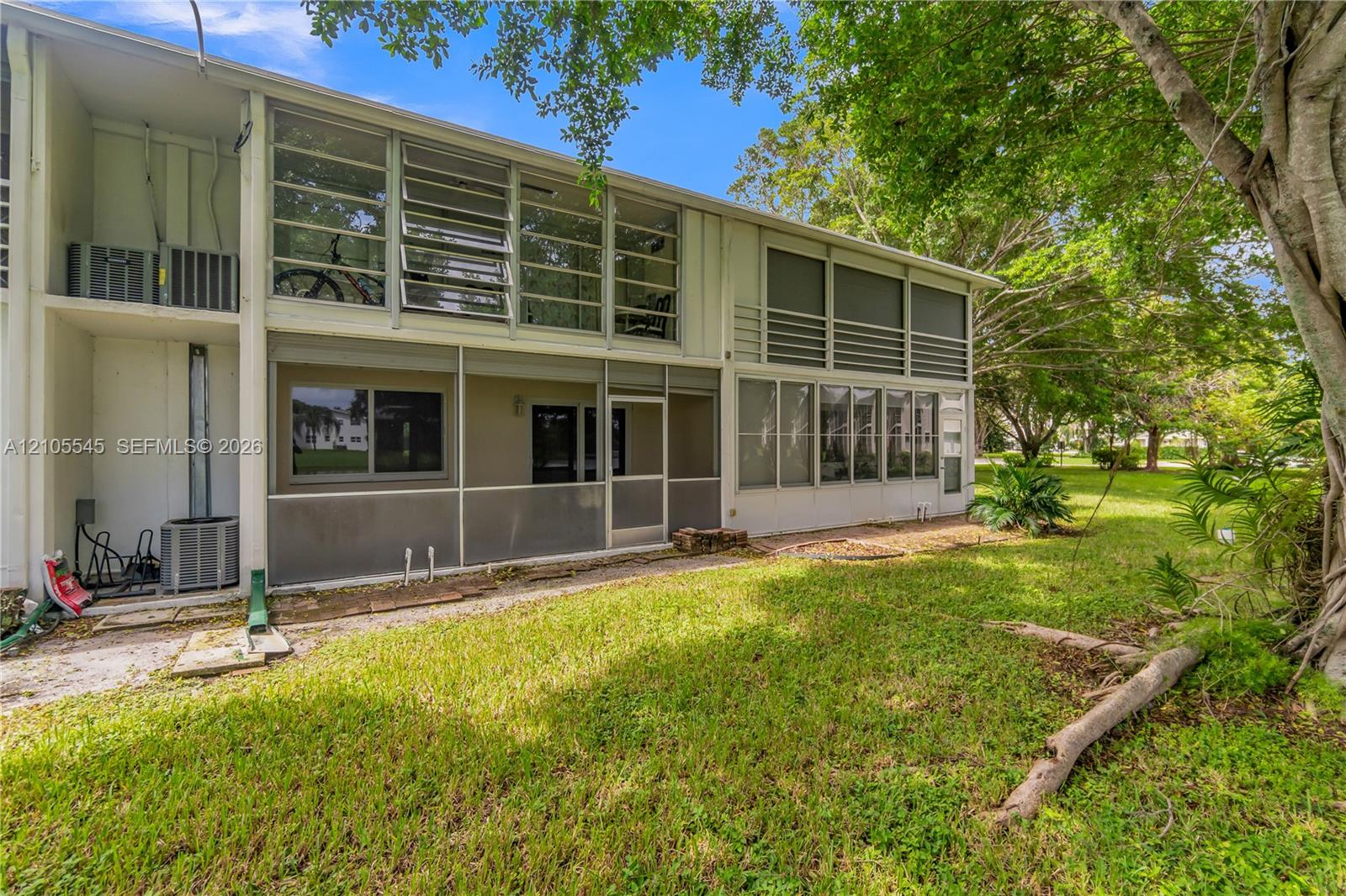 Multi-level property featuring screened enclosures, large jalousie windows, and a generous grassy area