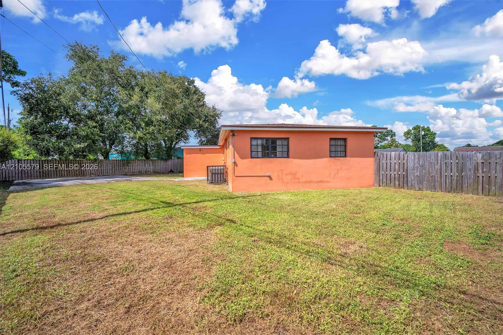 Exterior of the residence featuring a concrete masonry unit wall finish, rectangular grid windows, and an expansive rear yard enclosed by wooden perimeter fencing Exterior of the residence featuring a concrete masonry unit wall finish, rectangular grid windows, and an expansive rear yard enclosed by wooden perimeter fencing