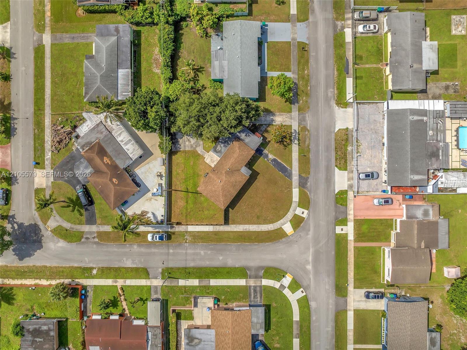 Aerial perspective featuring a corner lot orientation, paved street frontage, concrete sidewalks, and established landscaping