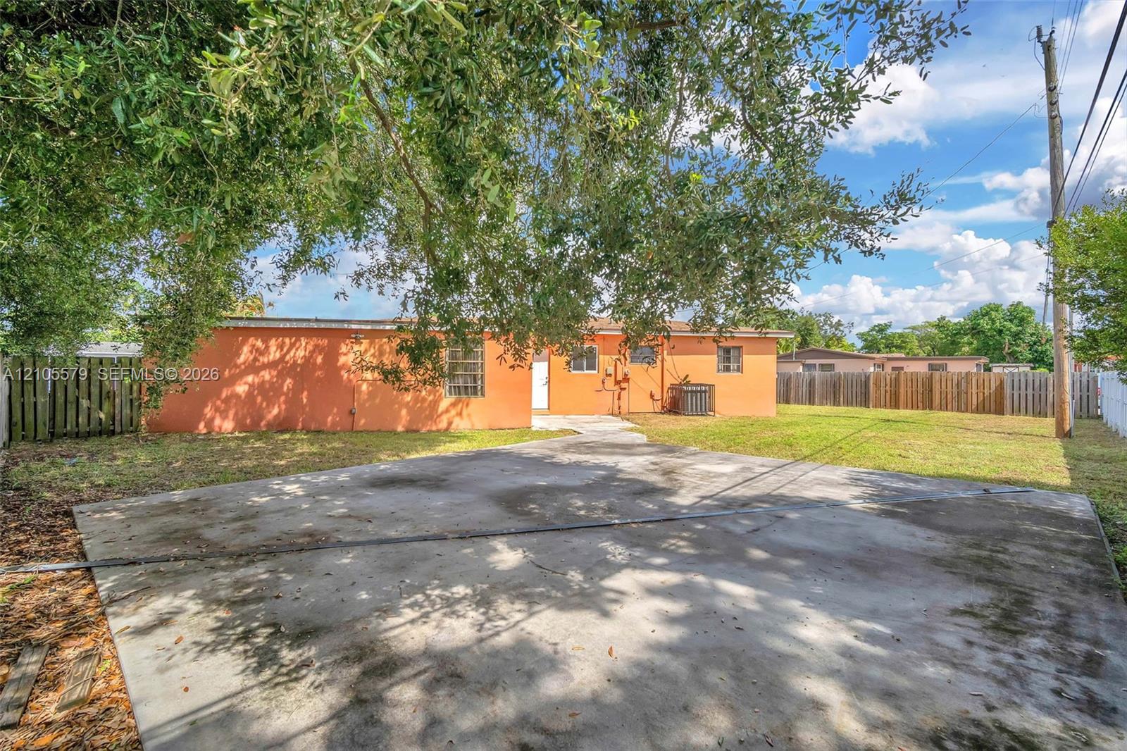 Stucco exterior featuring a concrete driveway, fenced perimeter, and mature canopy trees Stucco exterior featuring a concrete driveway, fenced perimeter, and mature canopy trees