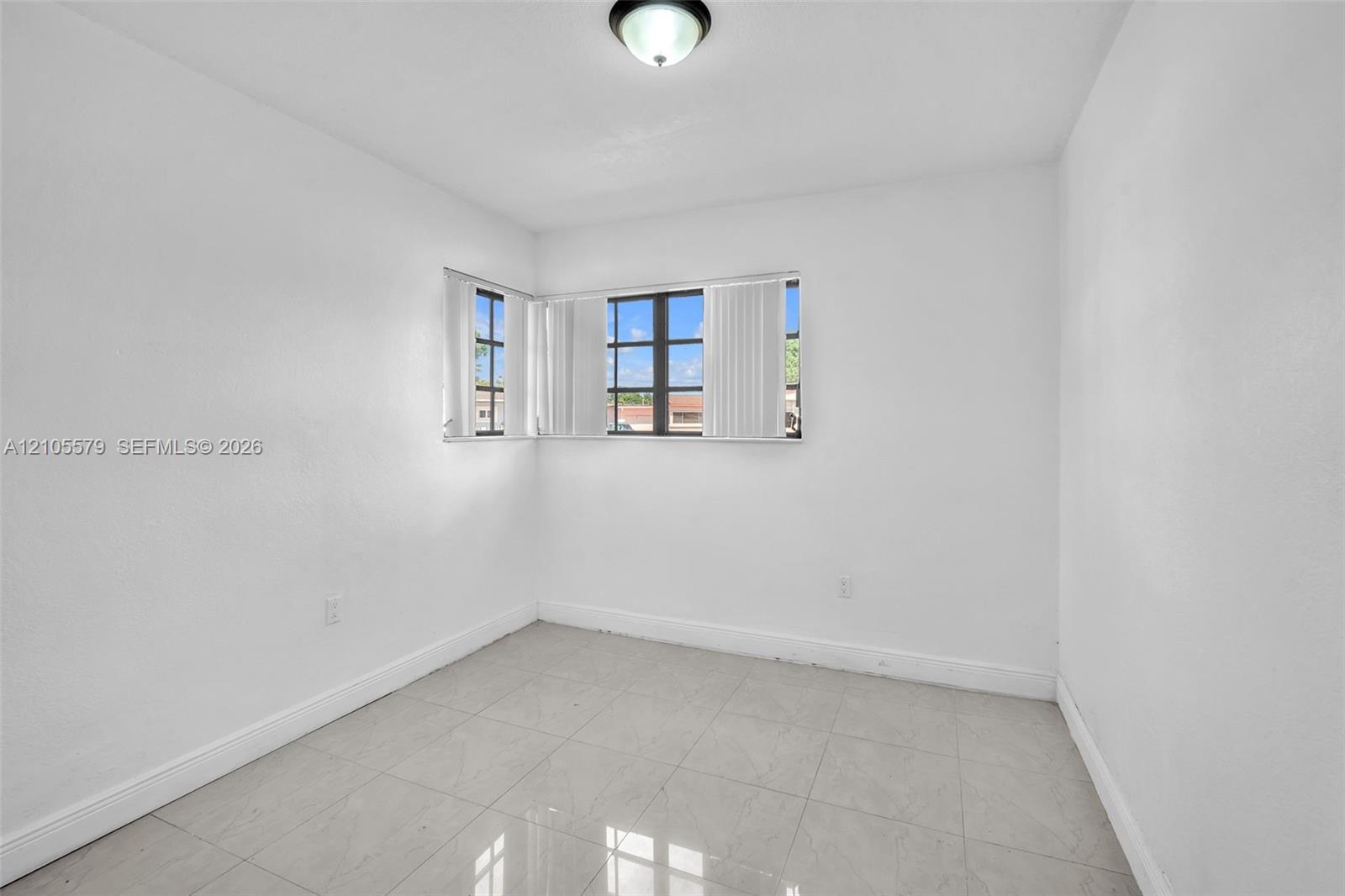 Neutral interior space featuring polished tile flooring, smooth white walls, corner-positioned multi-pane windows, and a flush-mount ceiling fixture