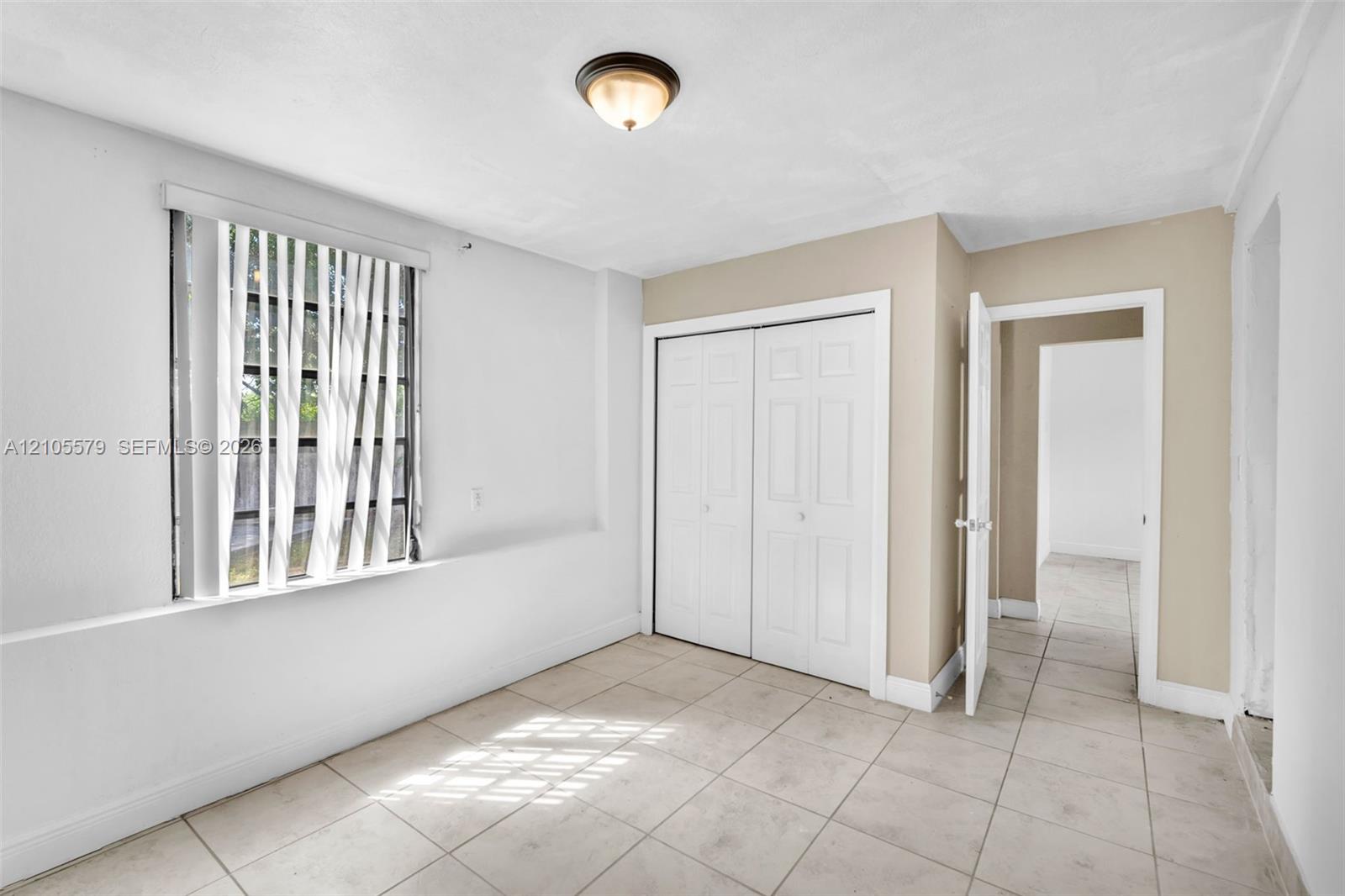 Neutral-toned interior featuring large-format tile flooring, a double-door closet with paneled doors, and a ceiling-mounted light fixture