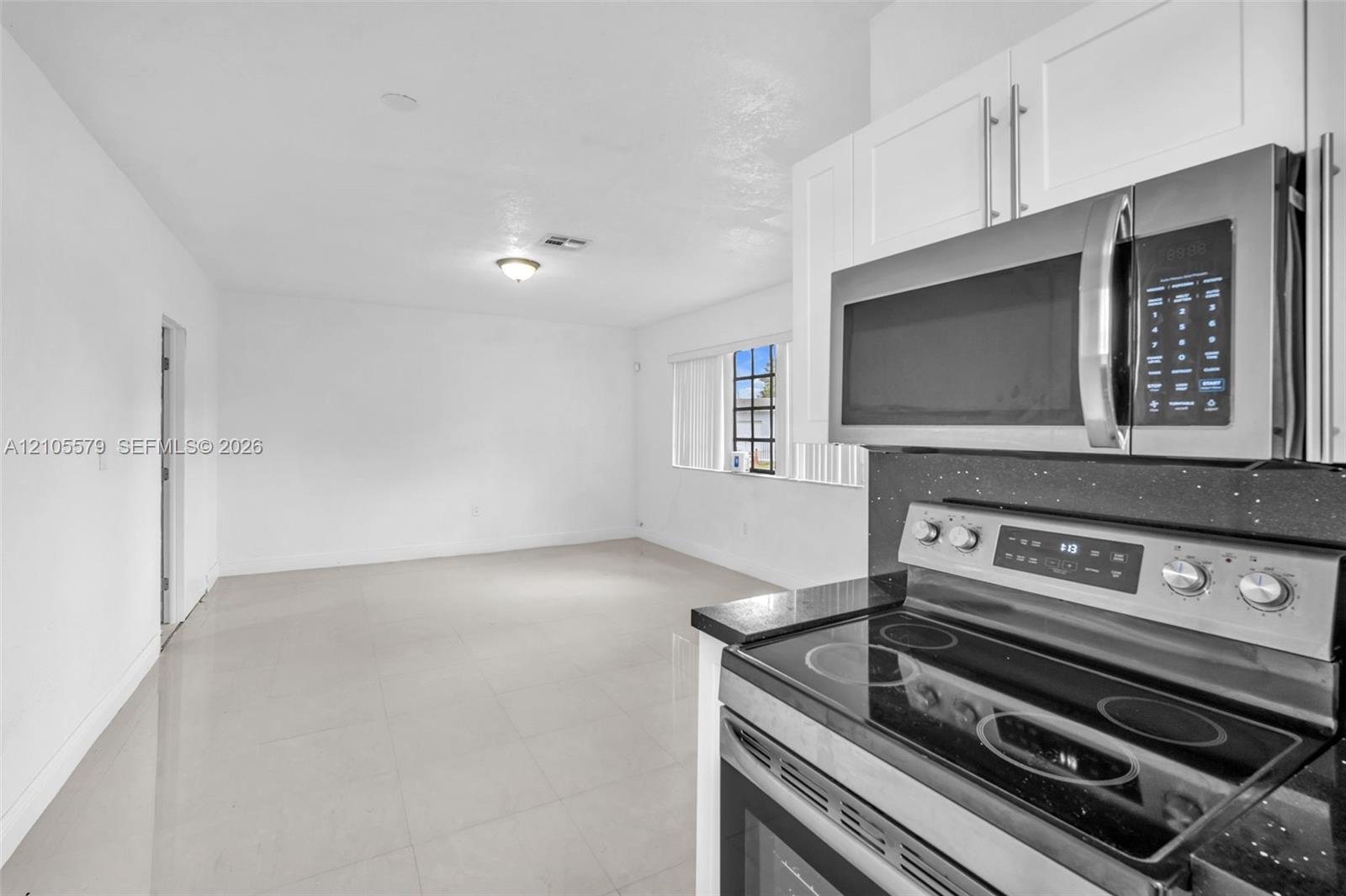 Kitchen featuring white shaker-style cabinetry, a stainless steel microwave, and a glass-top electric range with a dark solid-surface countertop