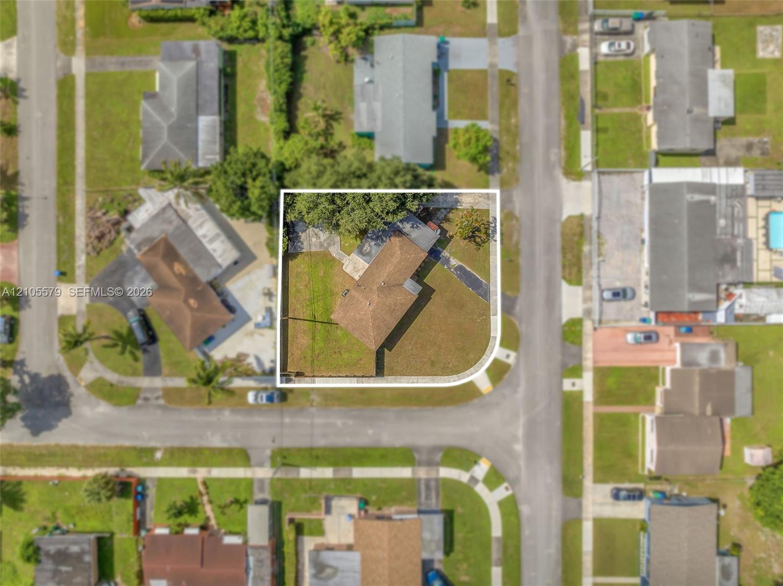 Corner lot featuring a multi-pitched shingled roof, paved driveway, and established trees within the fenced perimeter