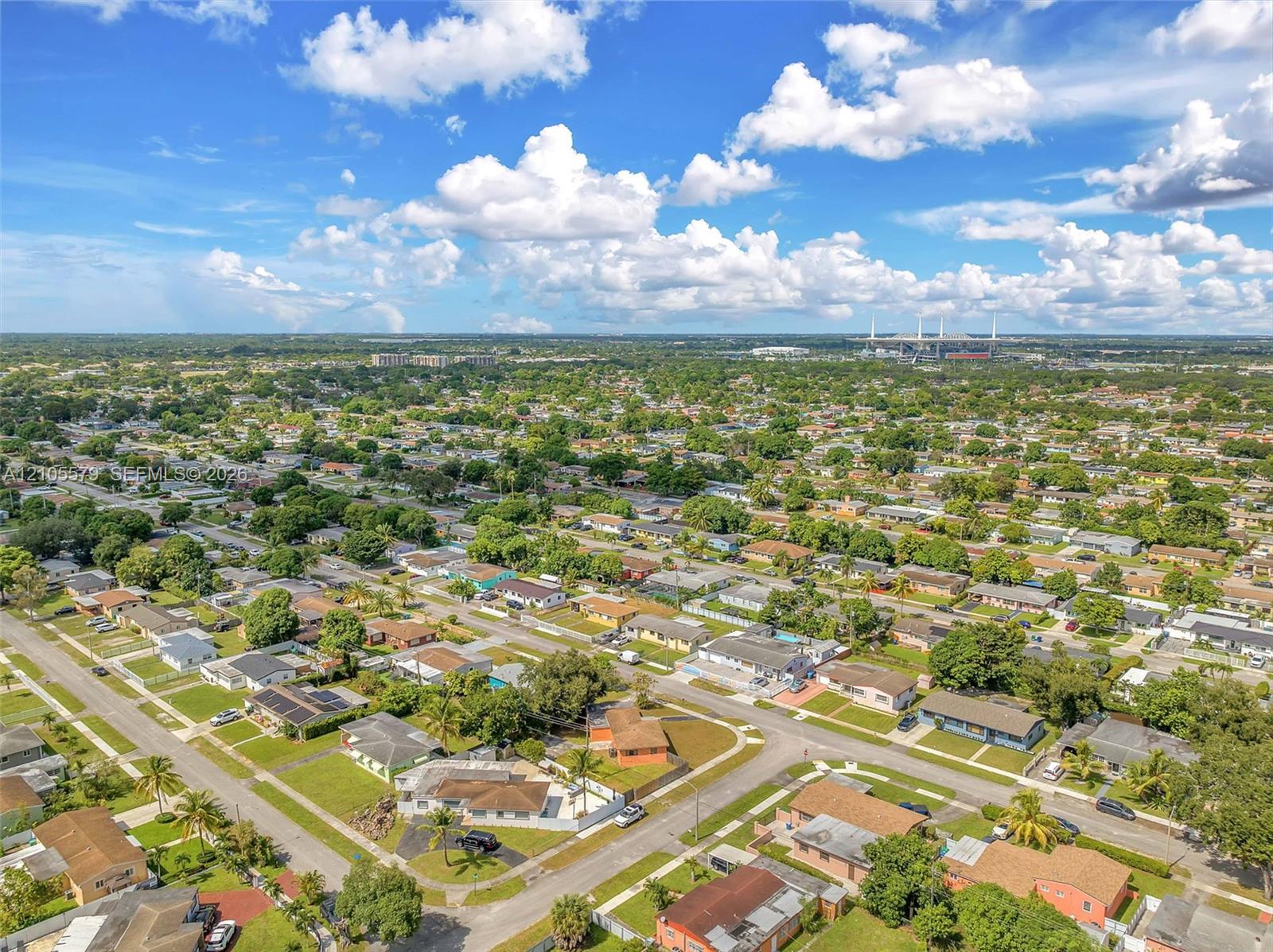 Aerial perspective of a residential landscape featuring mature trees, grid-patterned streets, single-story structures, and expansive green space