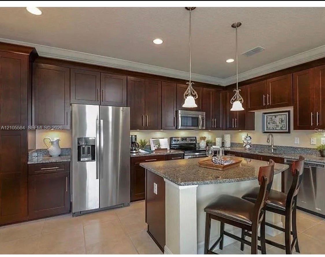 Kitchen featuring dark wood cabinetry, stone countertops, stainless steel appliances, a central island with bar seating, and pendant lighting