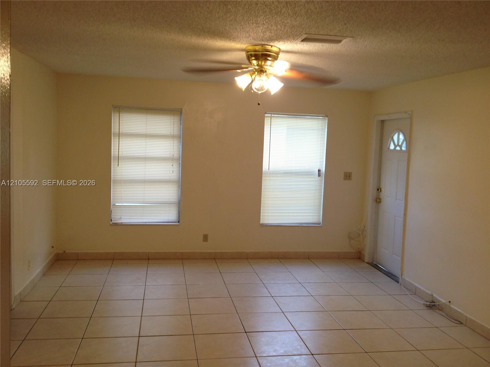 Tiled flooring, dual windows with blinds, ceiling fan with integrated lighting, and a paneled entry door