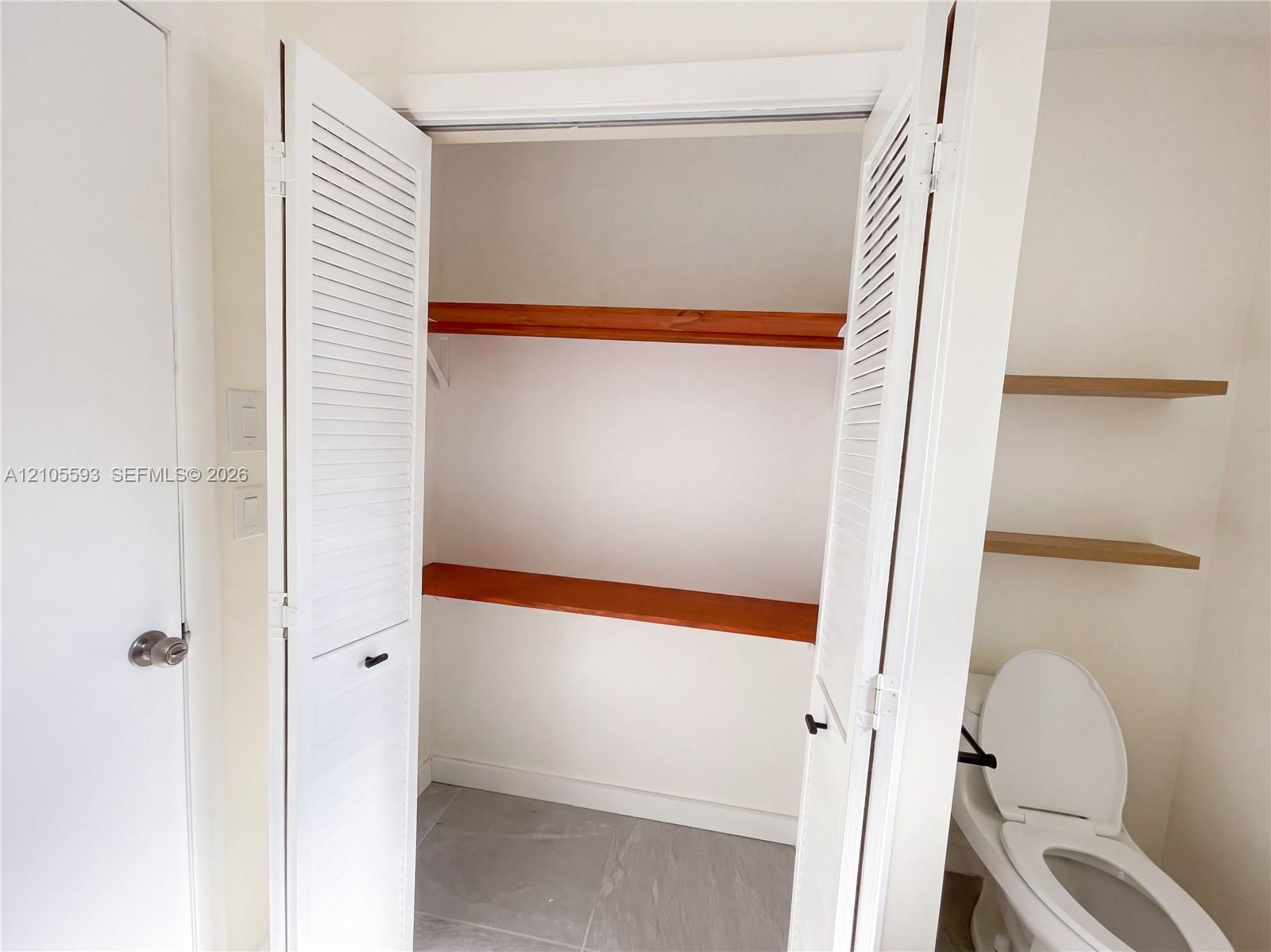 Double louvered closet doors, integrated wood shelving, tile flooring, and wall-mounted wood floating shelves