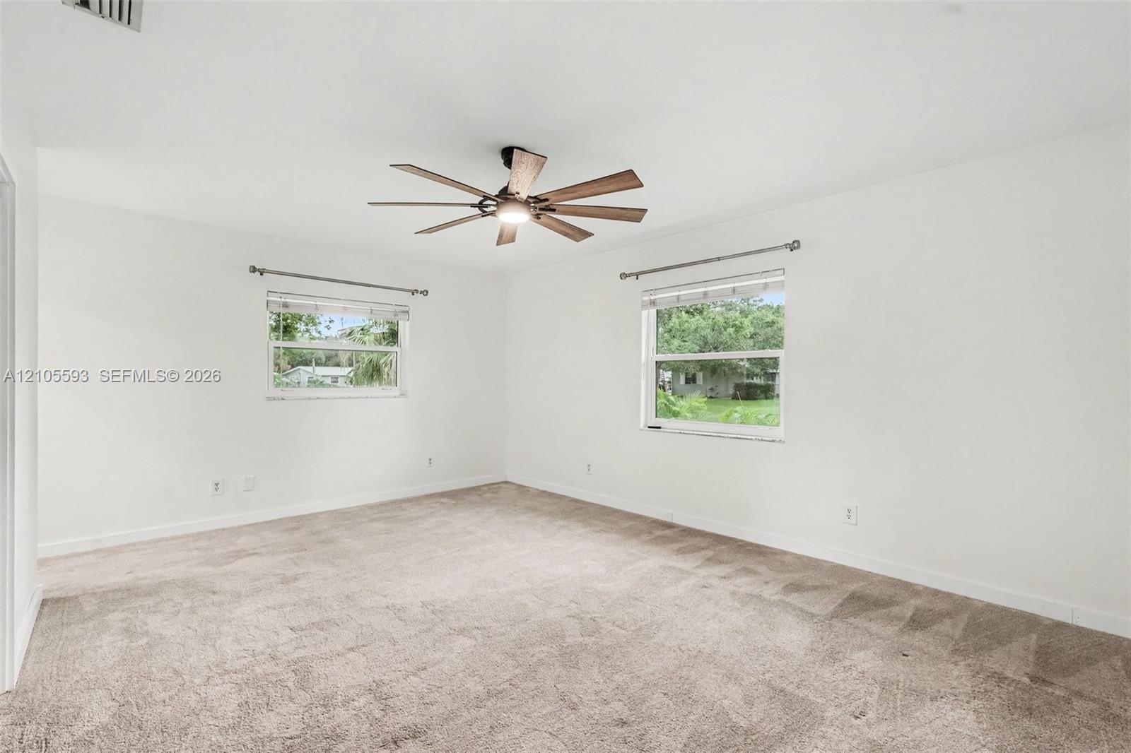 Neutral-toned wall-to-wall carpeting, ceiling fan with integrated lighting, dual windows with curtain hardware, and crisp white wall finishes