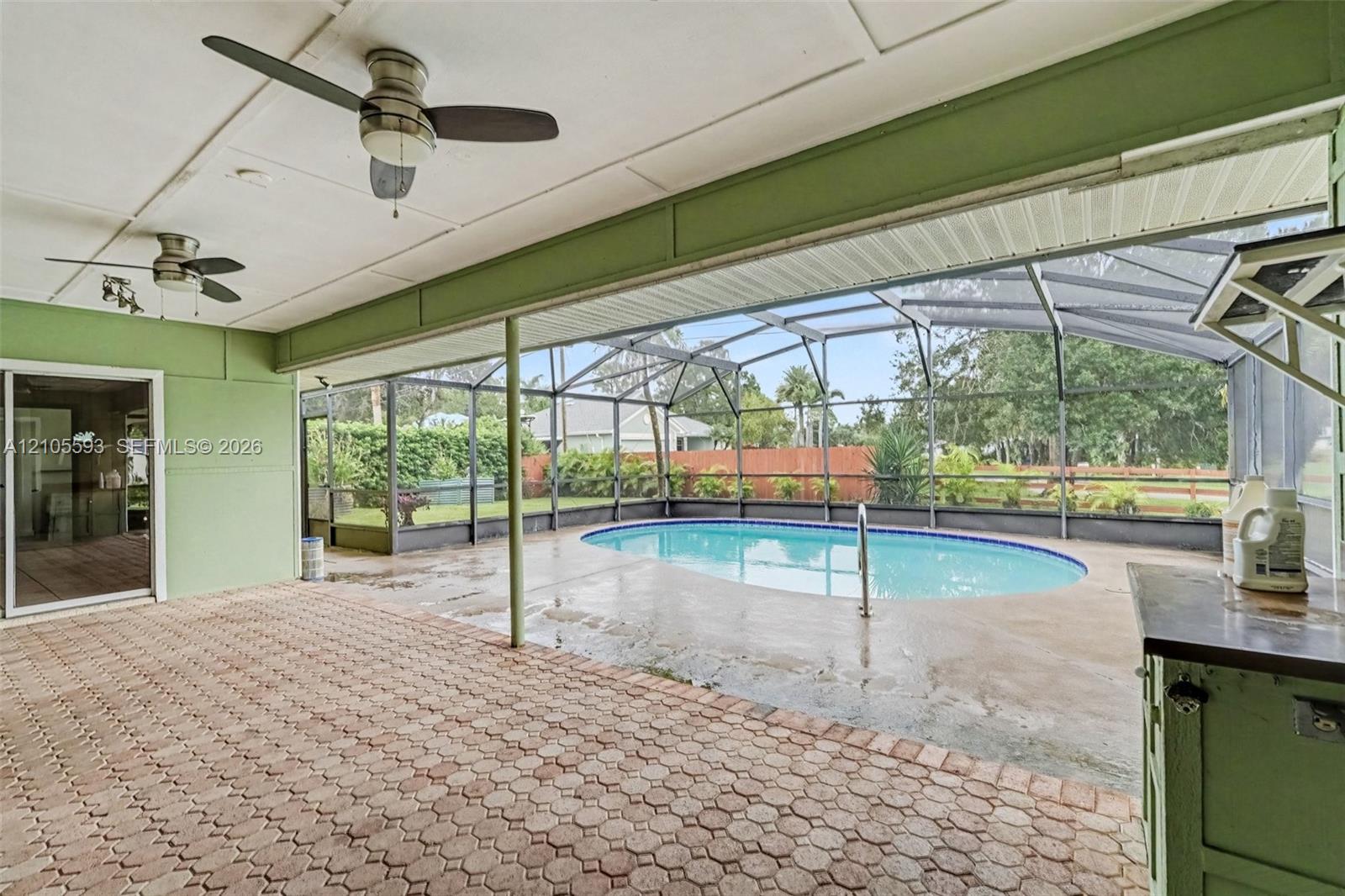 Covered patio featuring paver flooring, dual ceiling fans, a screened-in enclosure, and a swimming pool