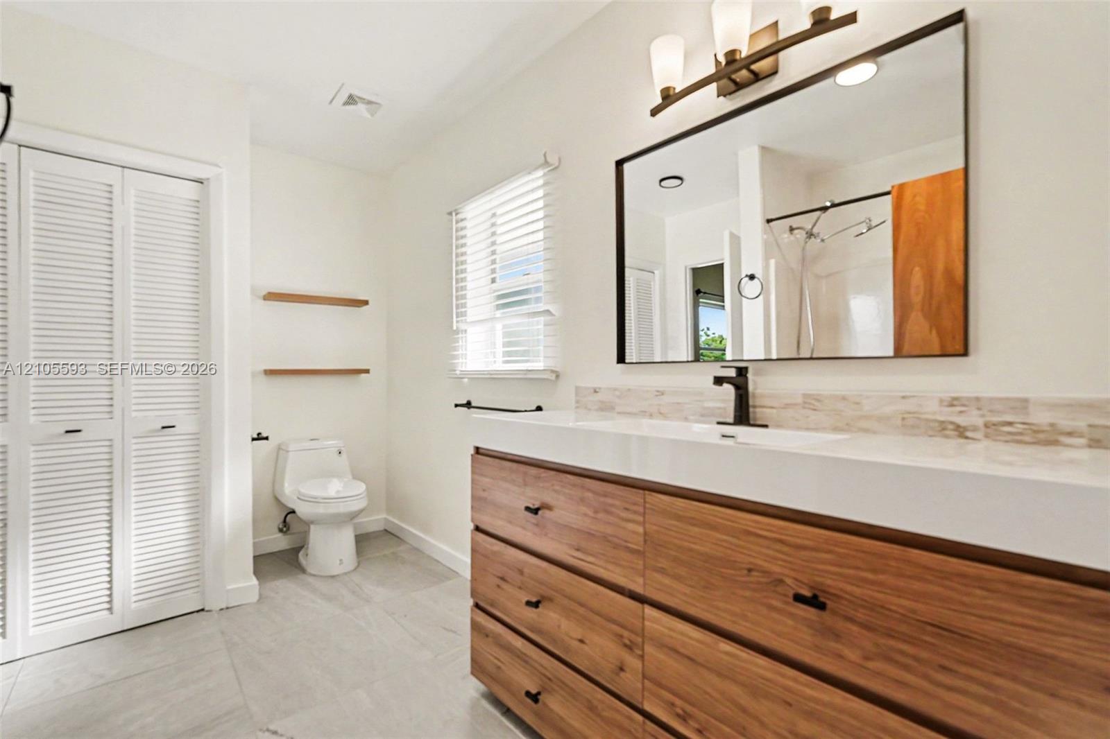 Bathroom featuring a wood-finish vanity with a rectangular sink, matte black faucet, framed mirror, and tile flooring