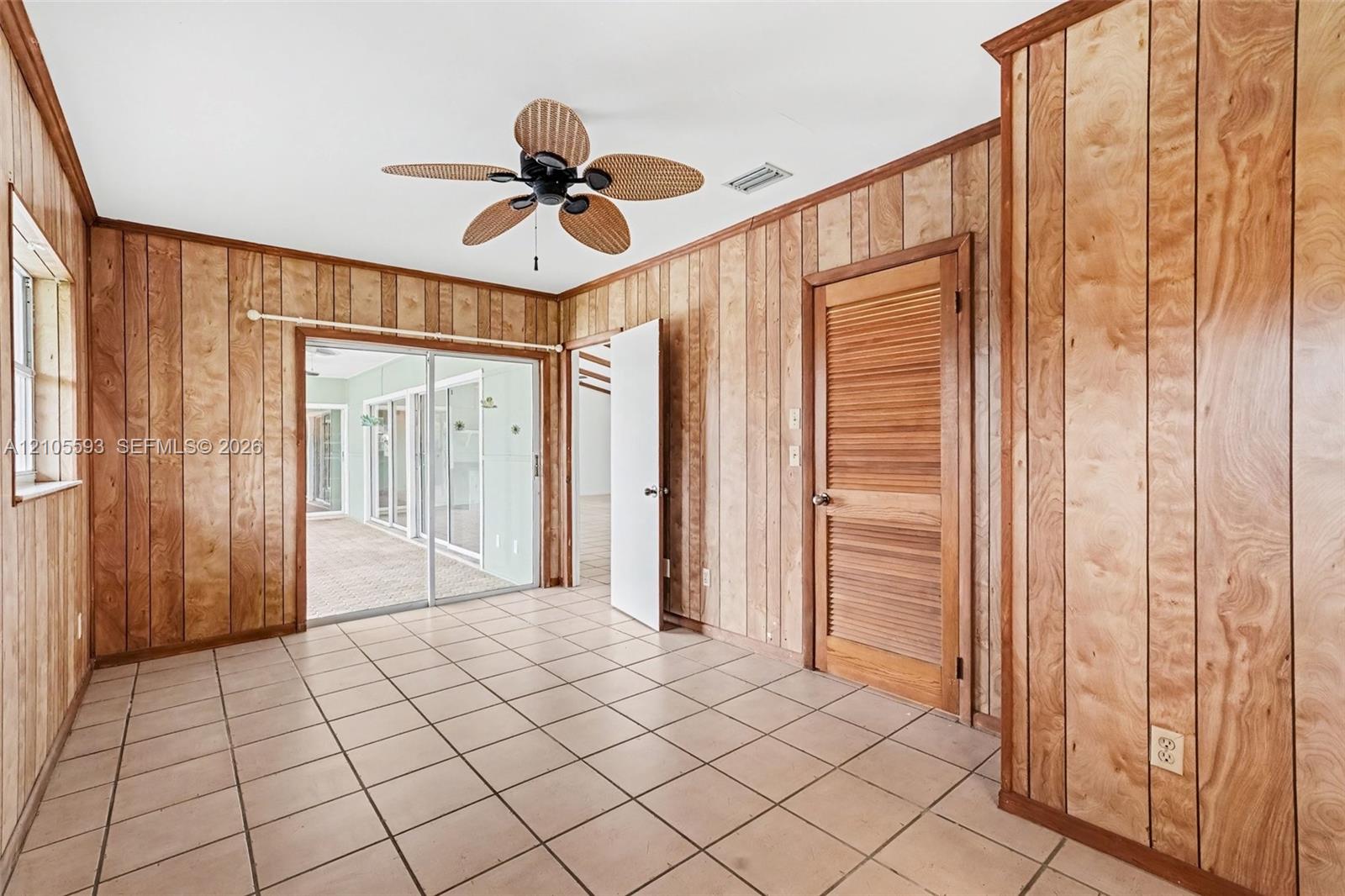 Wood-paneled wall finishes, tile flooring, louvered closet door, and ceiling fan