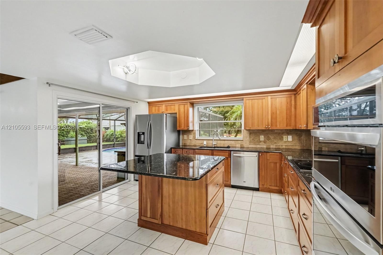 Kitchen featuring wood cabinetry, stone countertops, central island, stainless steel appliances, and tile flooring