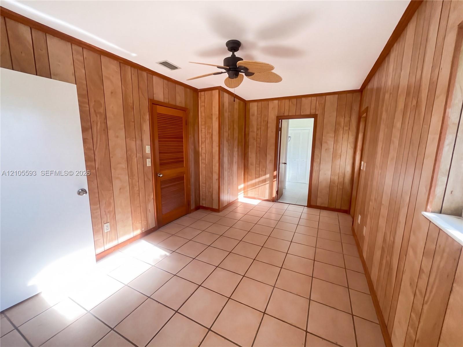 Interior room featuring wood-paneled walls, tile flooring, a louvered closet door, and a ceiling fan with integrated lighting