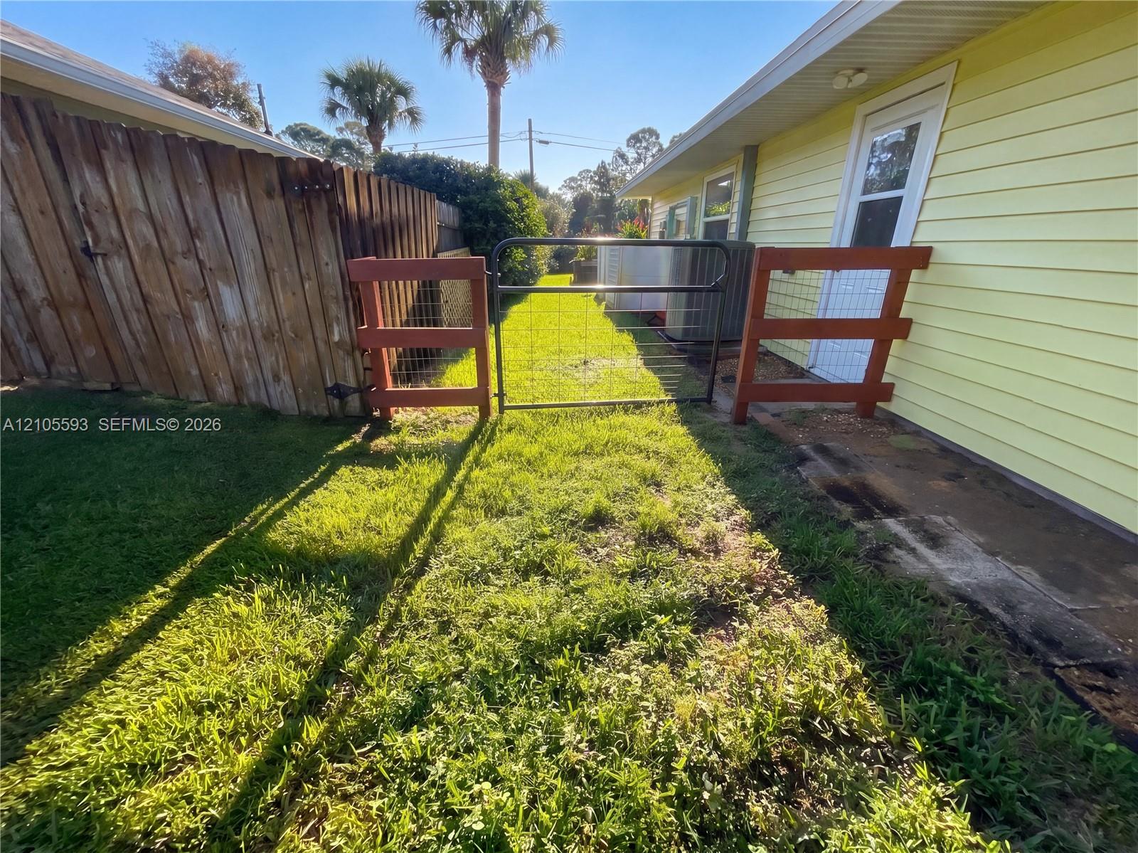 Exterior space featuring horizontal siding, a fenced side yard, a metal swing gate, and a concrete pathway