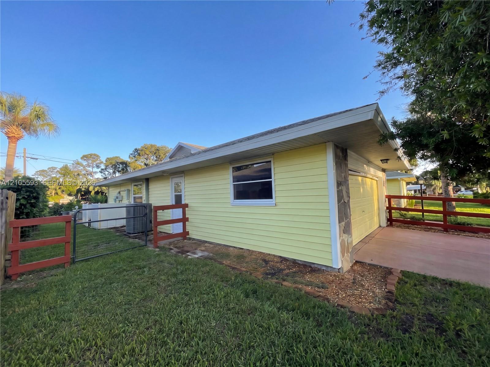 Exterior featuring yellow lap siding, stone masonry accents, a concrete driveway, and red-painted wooden post-and-rail fencing