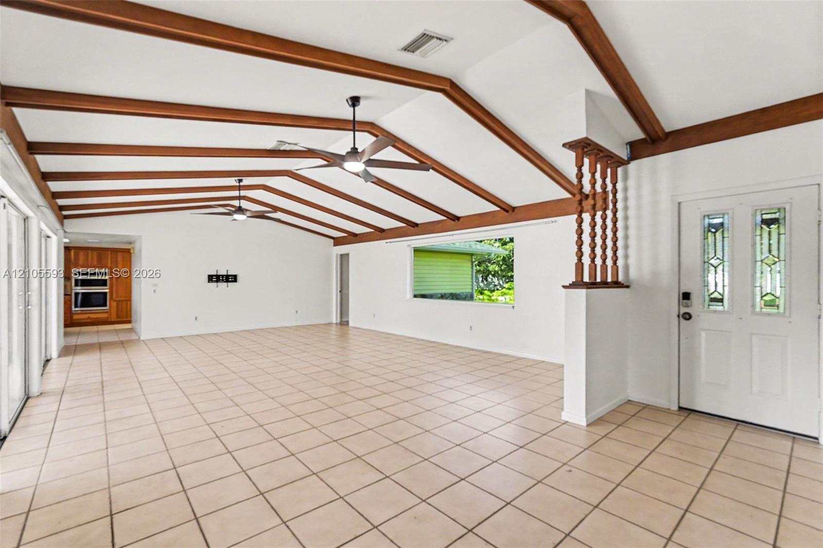 Vaulted ceiling featuring exposed wood beams, ceramic tile flooring, built-in dual wall ovens, ceiling fans, and an exterior door with glass panel inserts