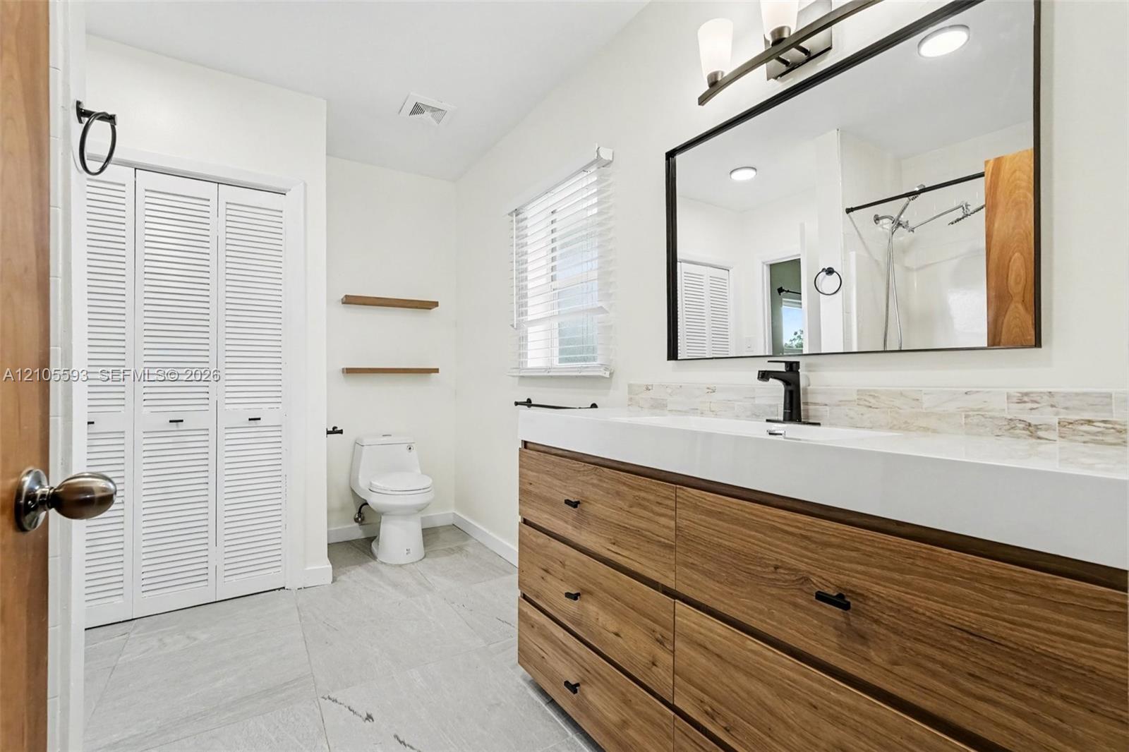 Bathroom featuring a wood-finish vanity with a rectangular sink, matte black faucet, wall-mounted mirror, and tile flooring