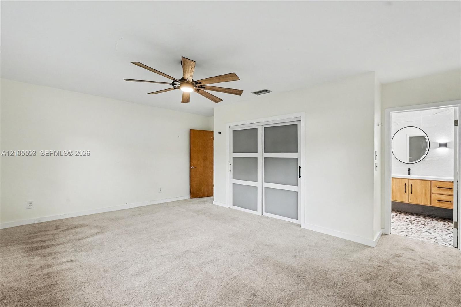 Room featuring neutral wall-to-wall carpeting, ceiling fan with integrated lighting, and dual-panel sliding doors with frosted glass inserts