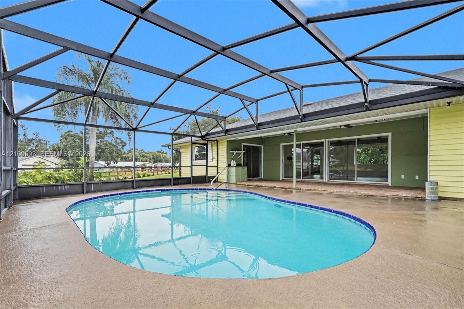 Screened-in patio featuring a concrete pool deck, private swimming pool with tile trim, and sliding glass door access to the residence