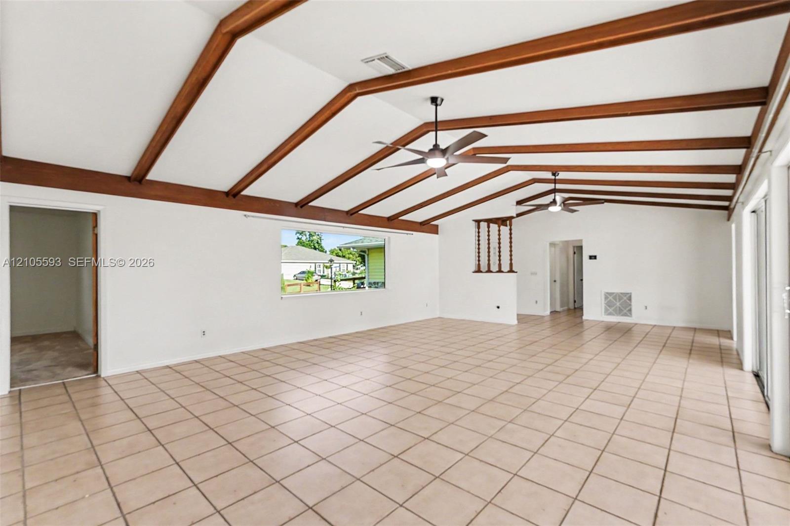 Vaulted ceiling featuring exposed wood beams, ceramic tile flooring, and dual ceiling fans