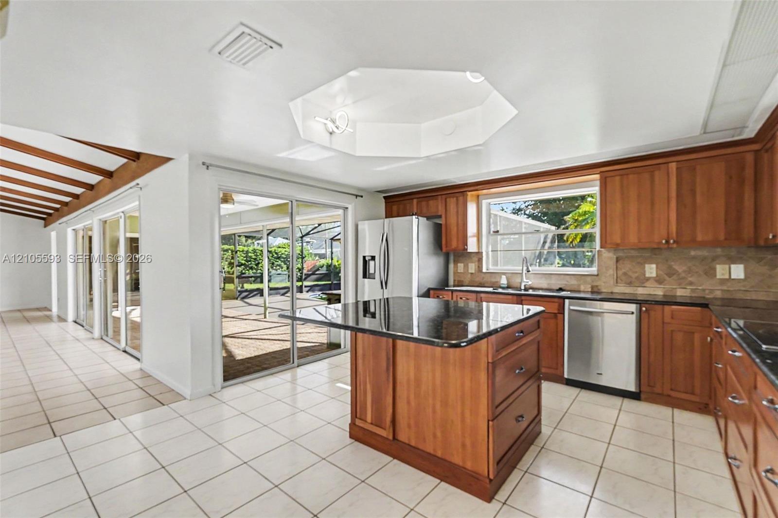 Kitchen featuring stained wood cabinetry, stone countertops, central island, tiled flooring, and vaulted ceiling with recessed lighting