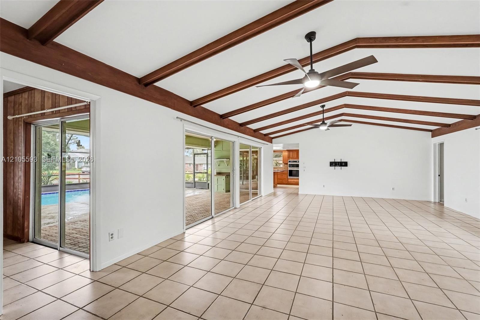 Vaulted ceiling featuring exposed wood beams, ceramic tile flooring, dual ceiling fans, and expansive sliding glass doors