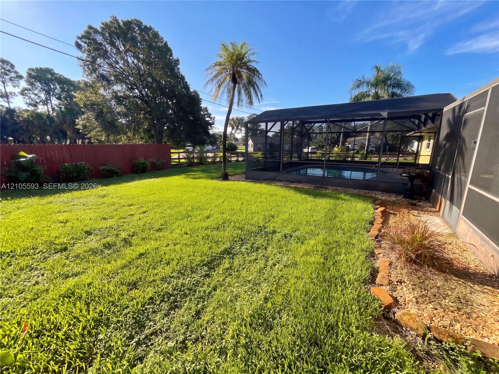 Backyard featuring a screened-in pool enclosure, stone-border landscaping, and a fenced perimeter