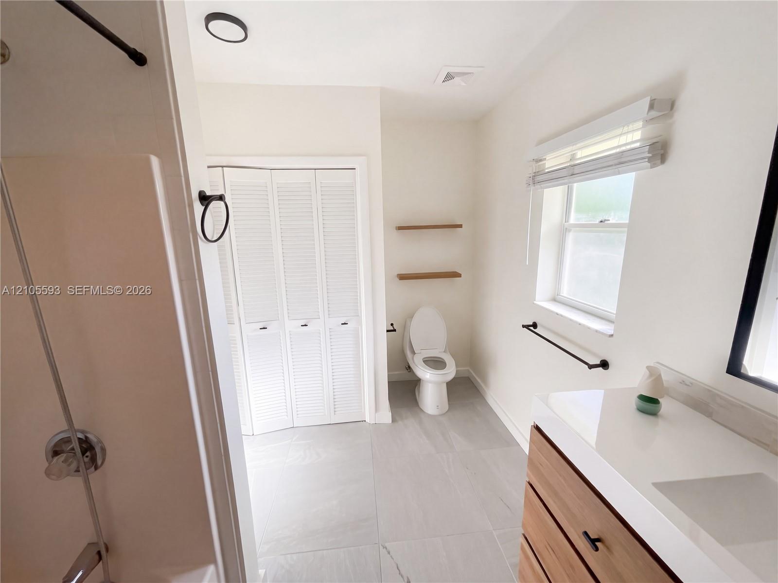 Bathroom featuring a vanity with a white countertop, wood-finish cabinetry, matte black hardware, large-format tile flooring, and a bifold closet
