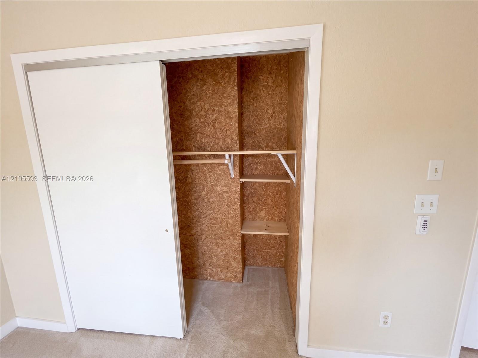 Sliding closet door with neutral wall finishes, interior storage shelving, and a wood-composite wall lining