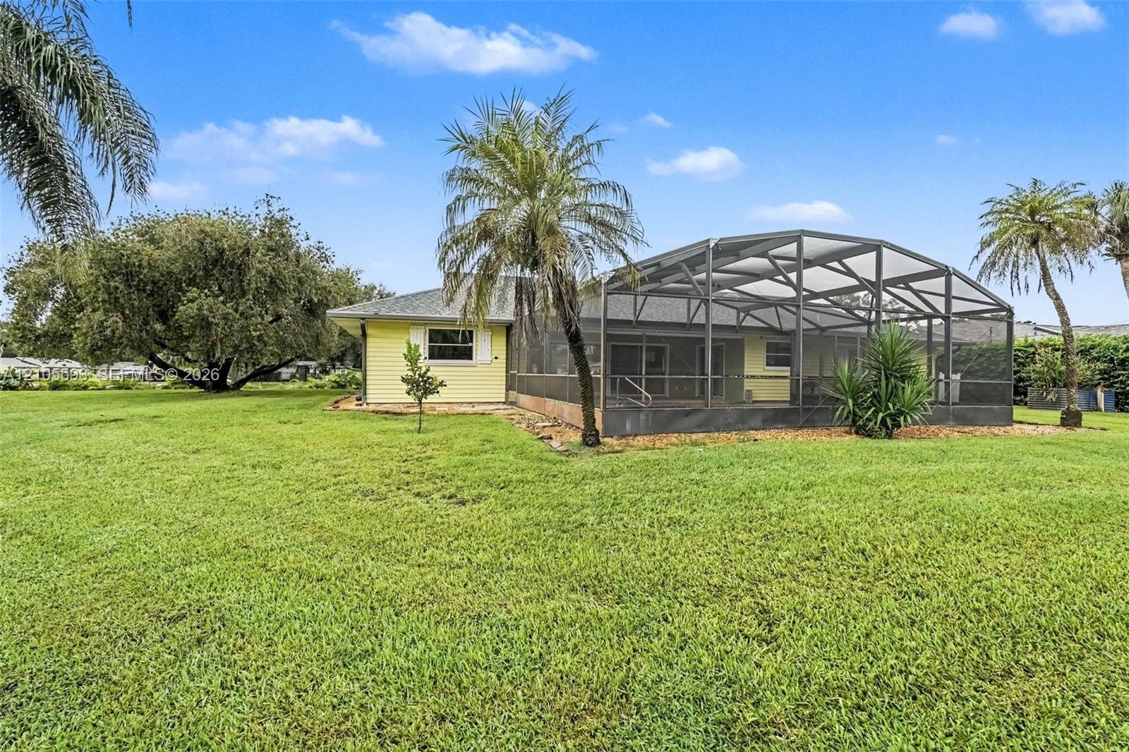 Exterior siding, screen-enclosed patio, and expansive lawn featuring mature trees and palms