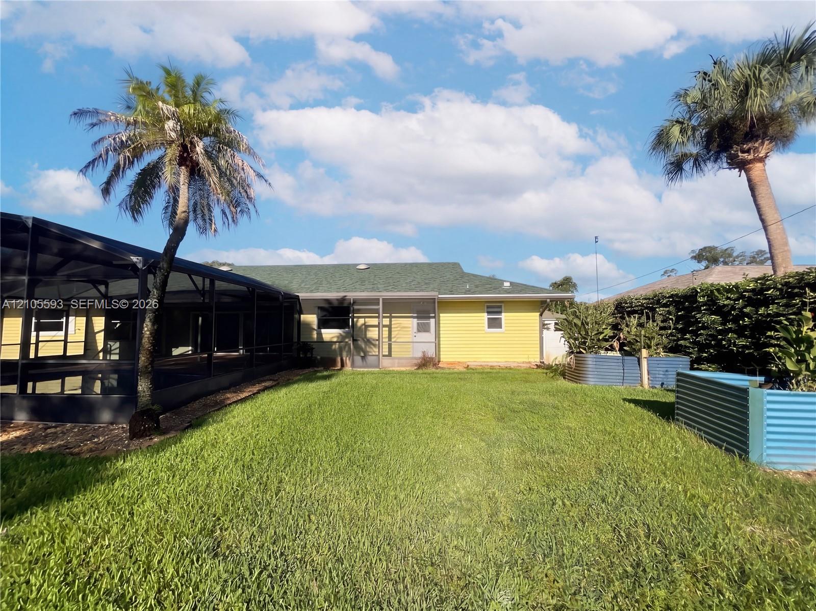 Backyard featuring a screened-in lanai, yellow horizontal siding, a green shingle roof, and corrugated metal garden beds