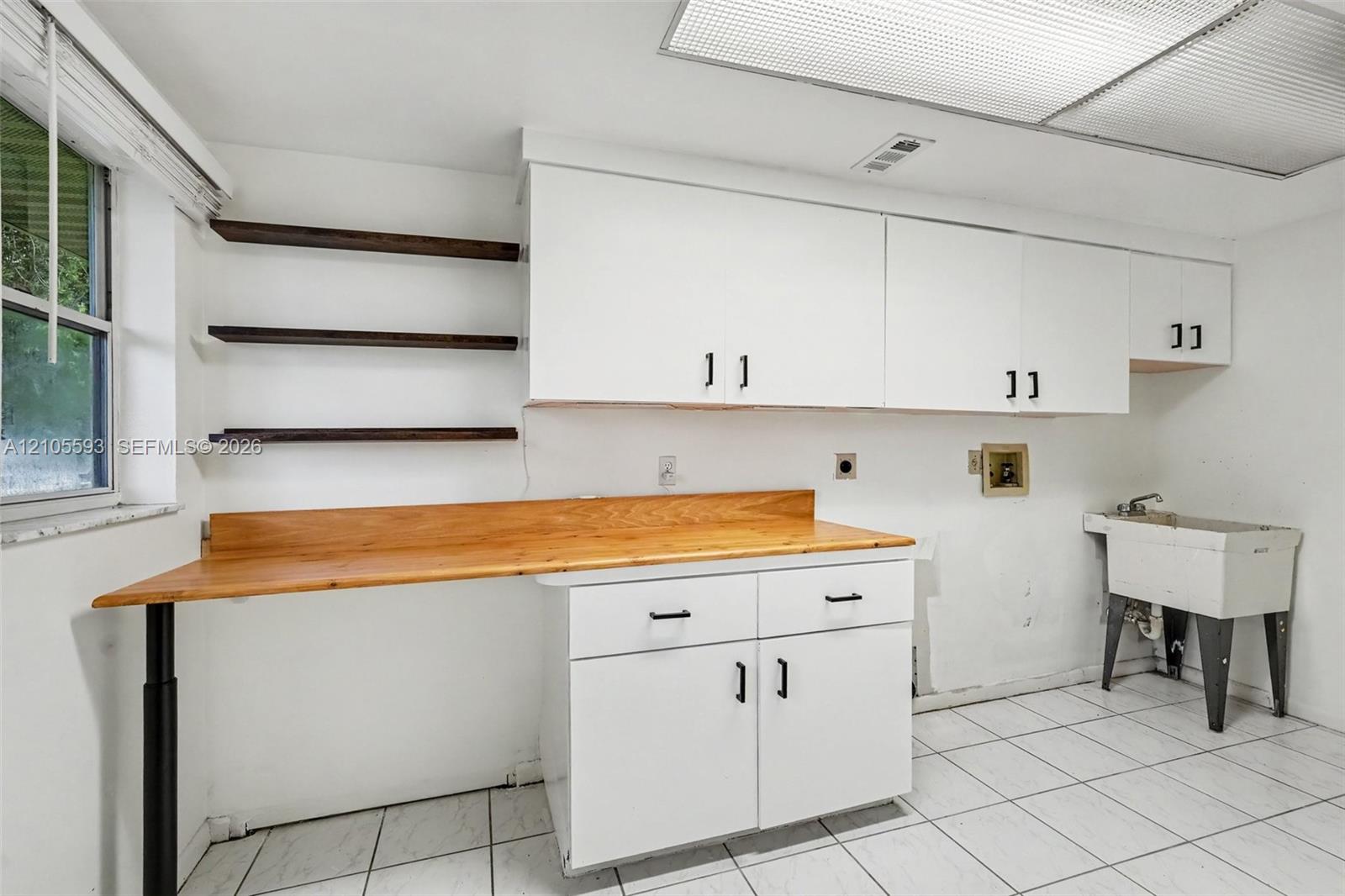 Work space featuring a wood-top counter, wall-mounted open shelving, white cabinetry, ceramic floor tiling, and a utility sink
