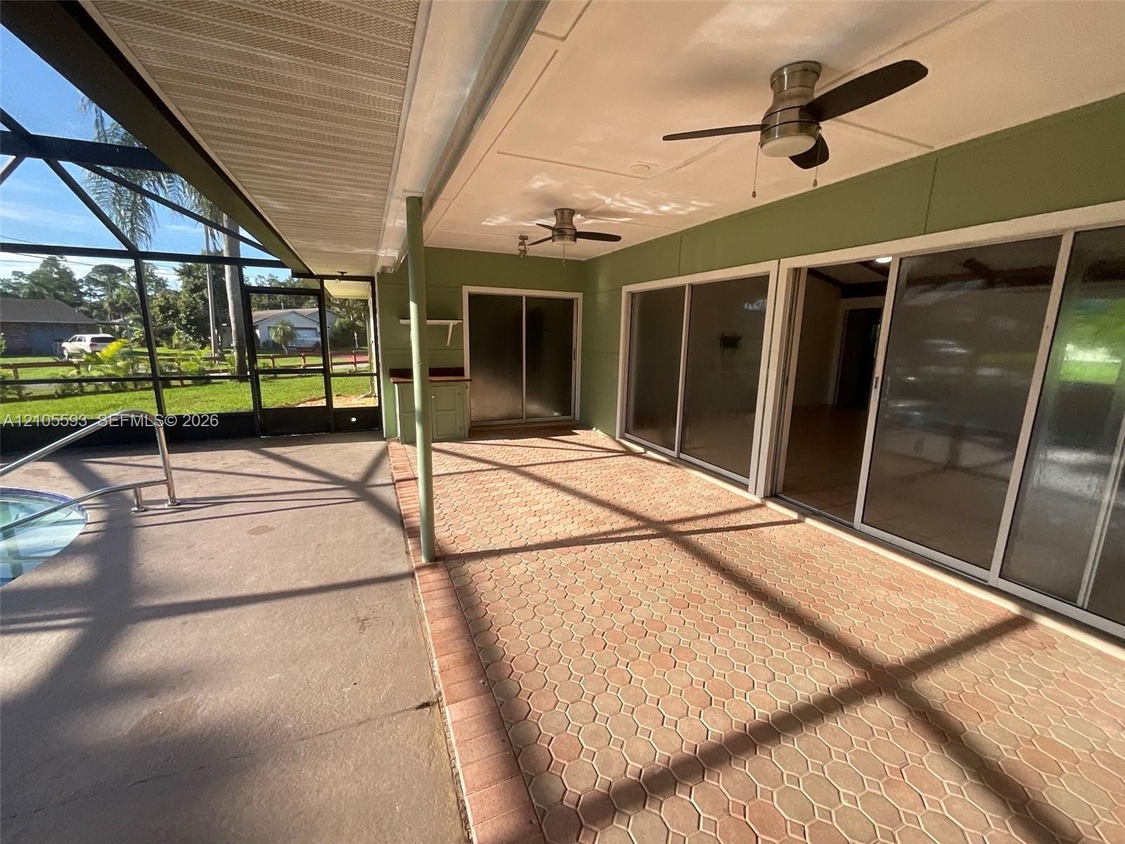 Screened-in lanai featuring paver flooring, dual ceiling fans, sliding glass doors, and an integrated pool area