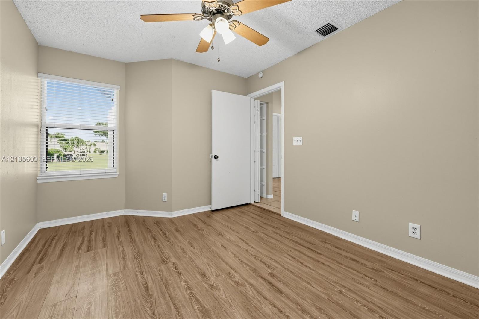 Neutral-toned interior space featuring wood-finish flooring, a multi-pane window, and a ceiling-mounted light fixture with a central fan Neutral-toned interior space featuring wood-finish flooring, a multi-pane window, and a ceiling-mounted light fixture with a central fan