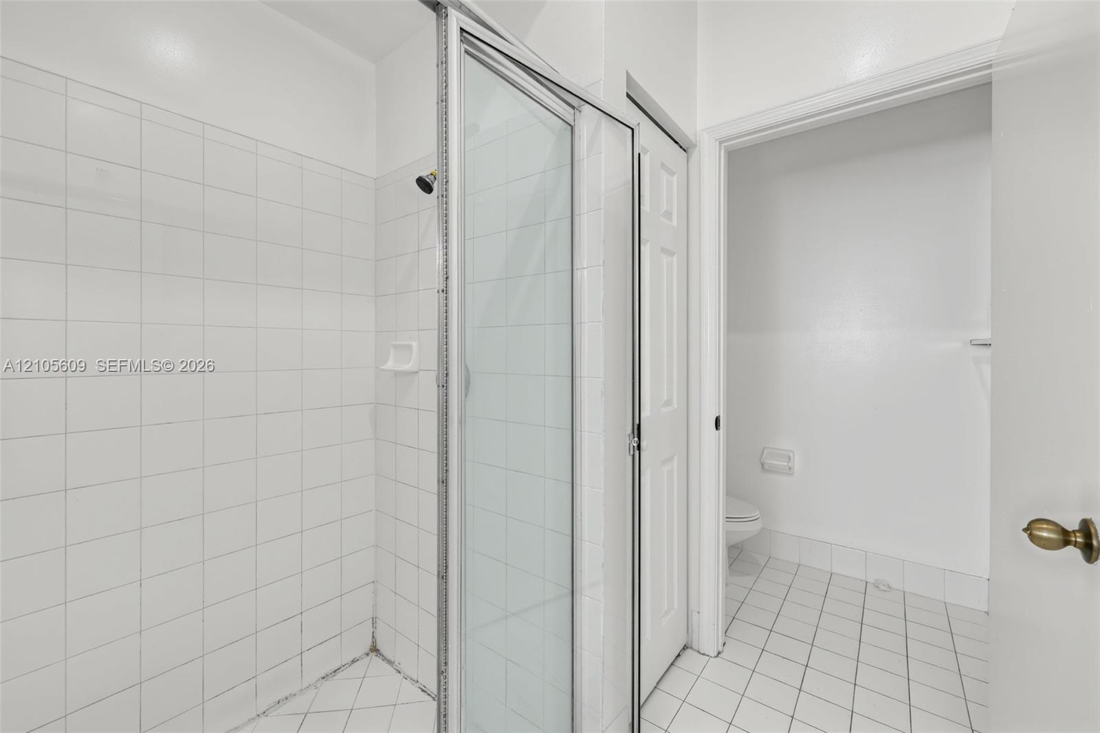 Shower stall with a glass door, white wall tiling, and white floor tiling