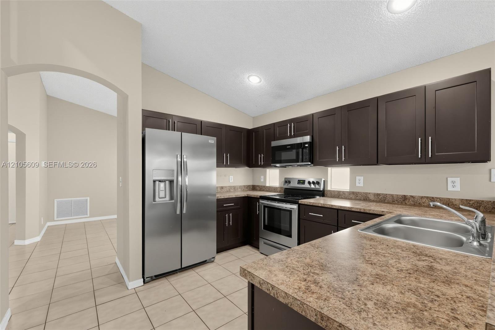 Kitchen featuring dark-toned cabinetry, stainless steel appliances, expansive stone-finish countertops, recessed lighting, and tile flooring Kitchen featuring dark-toned cabinetry, stainless steel appliances, expansive stone-finish countertops, recessed lighting, and tile flooring
