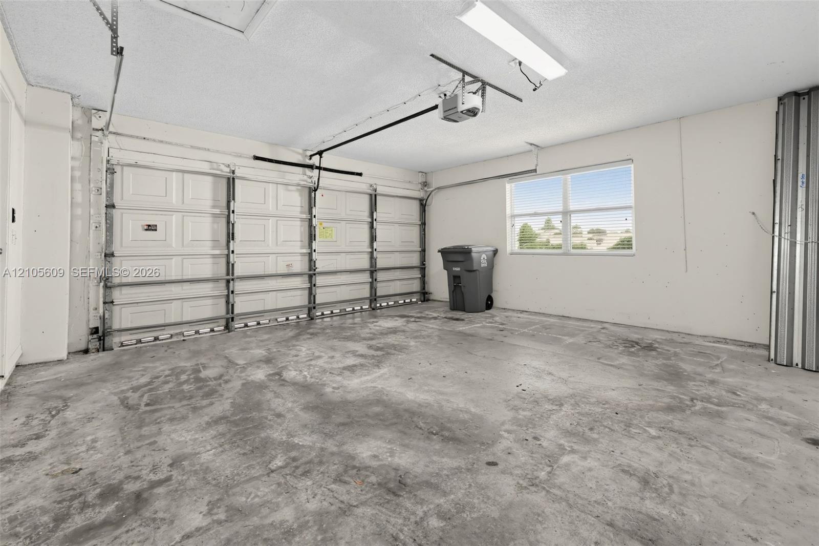 Enclosed multi-car garage featuring a sectional metal door, concrete flooring, overhead light fixture, and a window with exterior exposure