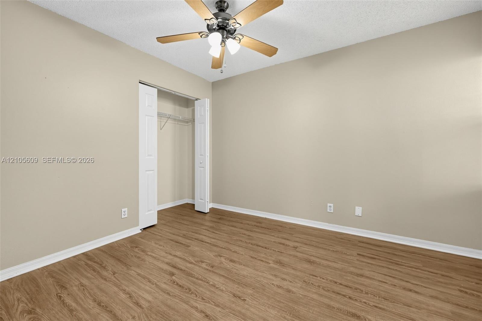 Room featuring wood-finish flooring, neutral wall paint, a ceiling fan with integrated lighting, and a closet with bifold doors Room featuring wood-finish flooring, neutral wall paint, a ceiling fan with integrated lighting, and a closet with bifold doors