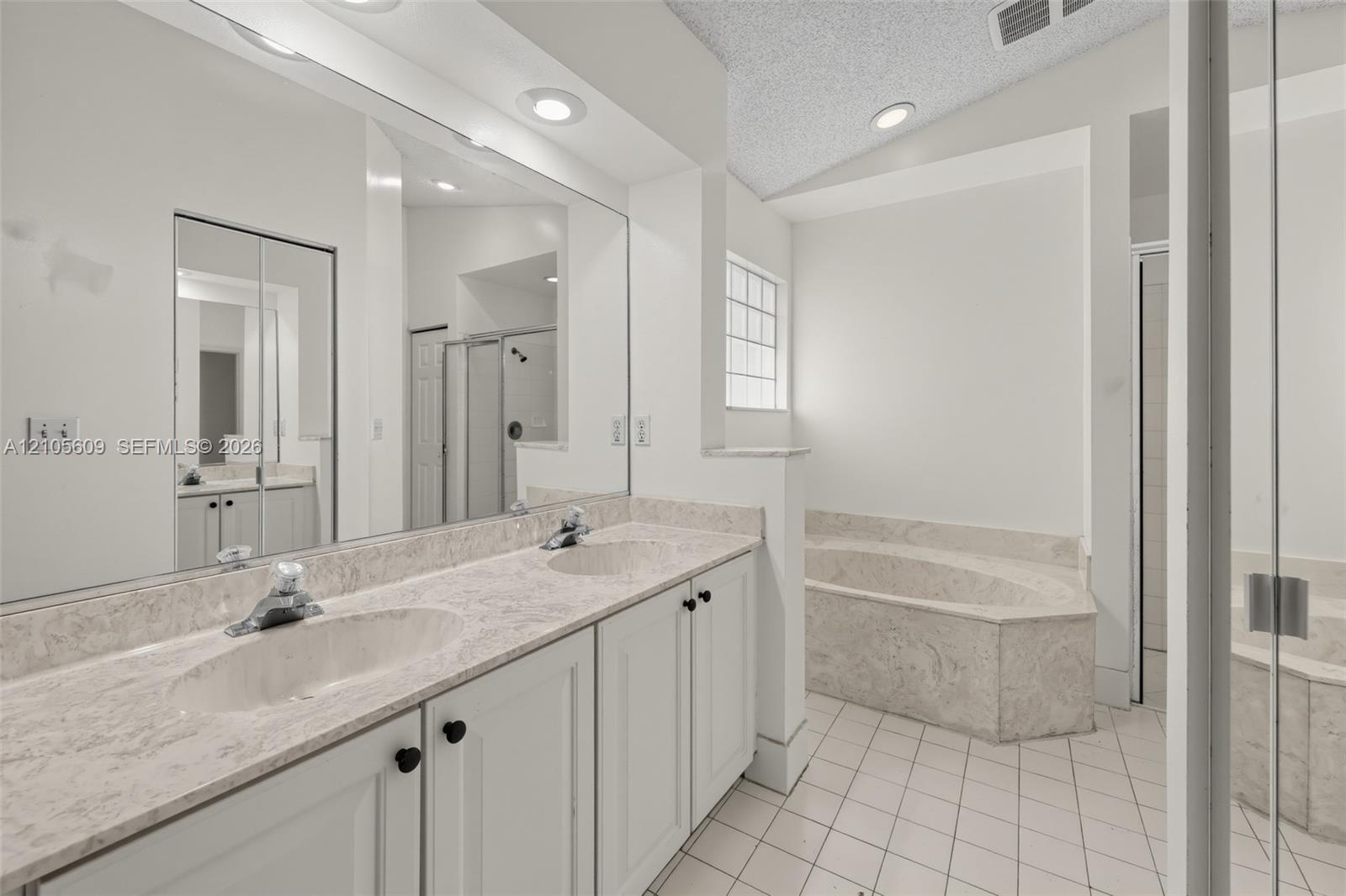 Dual-sink vanity with stone-finish countertop, full-width mirror, recessed lighting, and separate built-in soaking tub with surround