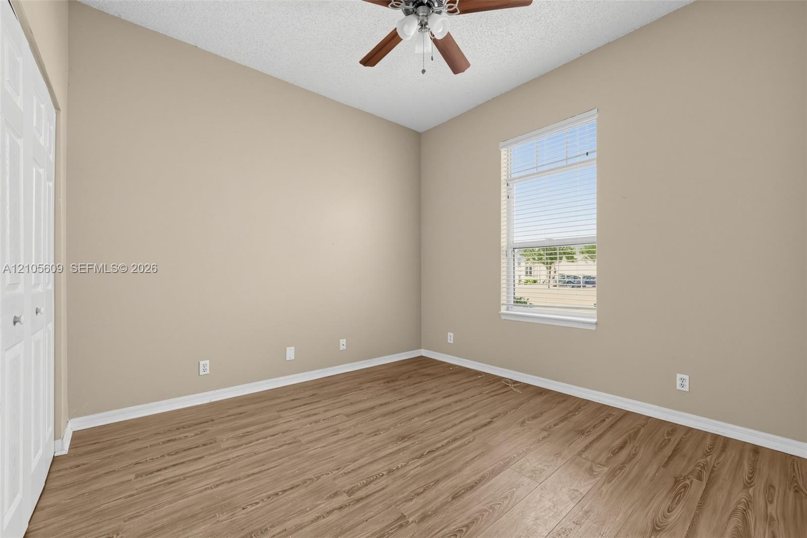 Room featuring wood-finish flooring, a ceiling fan with integrated lighting, textured ceiling, and double-door closet cabinetry Room featuring wood-finish flooring, a ceiling fan with integrated lighting, textured ceiling, and double-door closet cabinetry