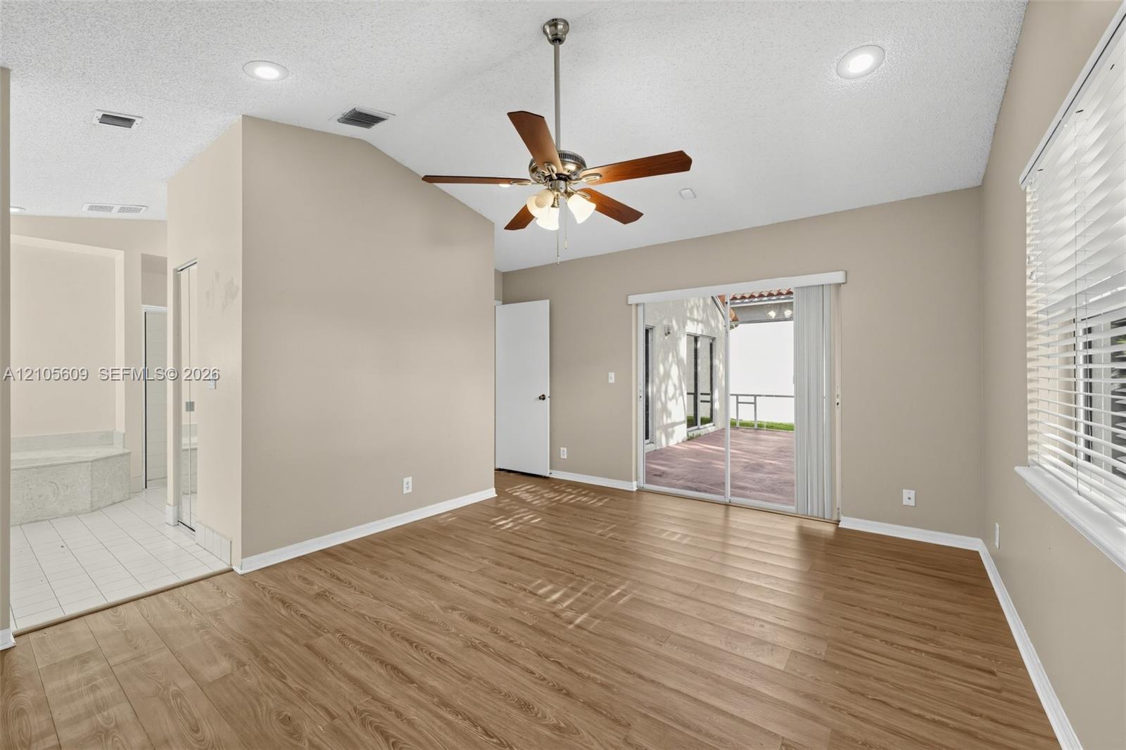 Vaulted ceiling with recessed lighting and a brushed-nickel ceiling fan, wood-finish flooring, and sliding glass doors