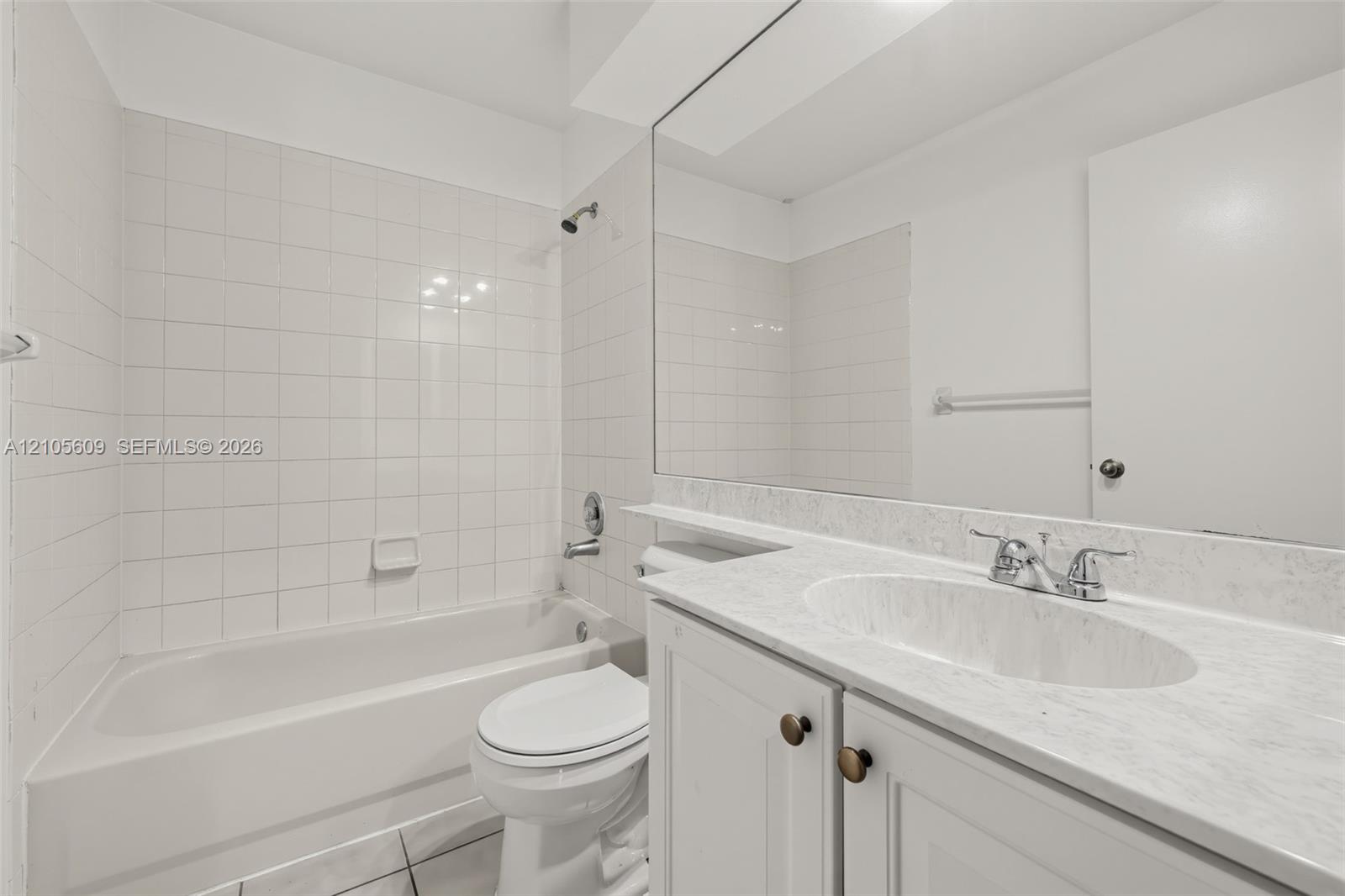 Bathroom featuring a white bathtub with a tile surround, vanity with a light-toned stone-patterned countertop, integrated oval sink, and a full-width wall mirror