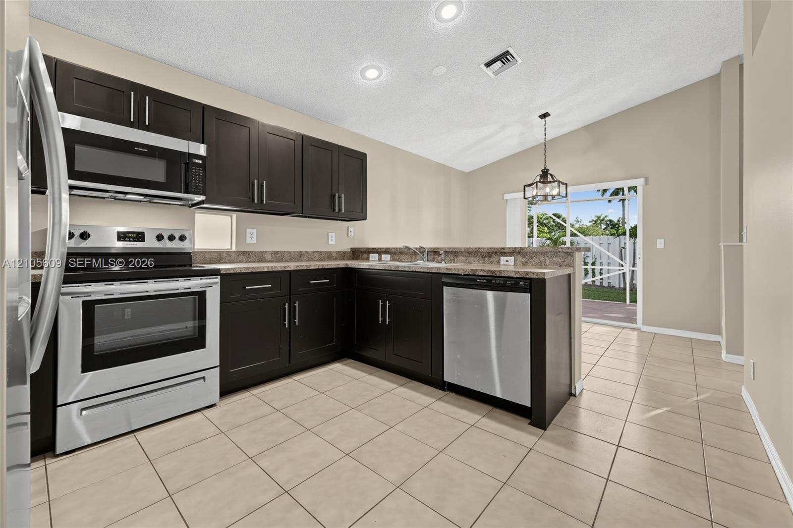 Kitchen featuring dark wood-finish cabinetry, stone-finish countertops, stainless steel appliances, tile flooring, and vaulted ceilings Kitchen featuring dark wood-finish cabinetry, stone-finish countertops, stainless steel appliances, tile flooring, and vaulted ceilings