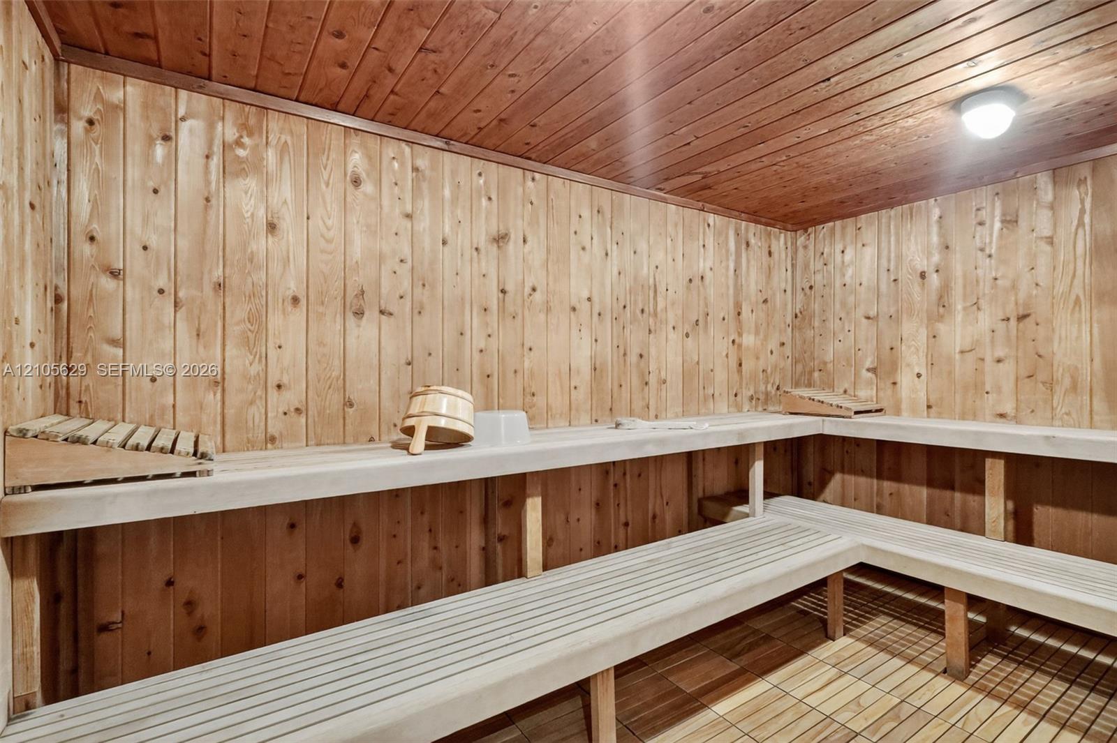 Sauna featuring tongue-and-groove wood paneling, multi-level slatted benches, tile flooring, and a flush-mount ceiling light fixture