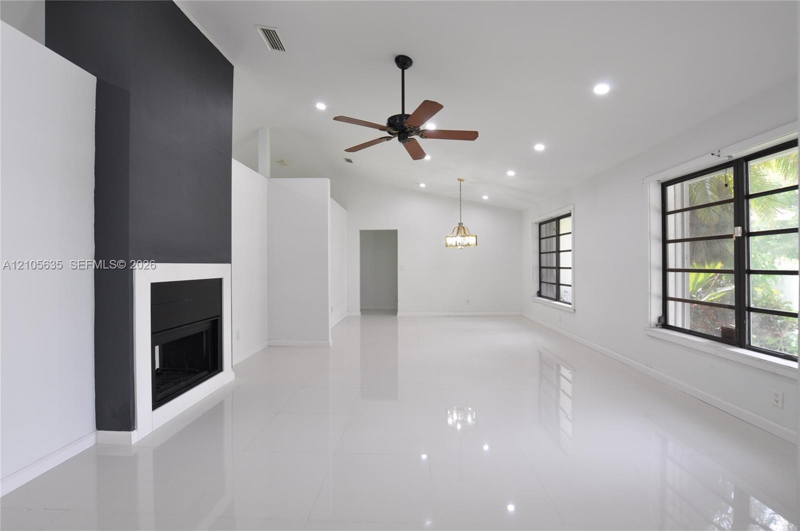 Living area featuring high vaulted ceilings, large-format polished tile flooring, a floor-to-ceiling accent fireplace, recessed lighting, and a multi-pane grid window system