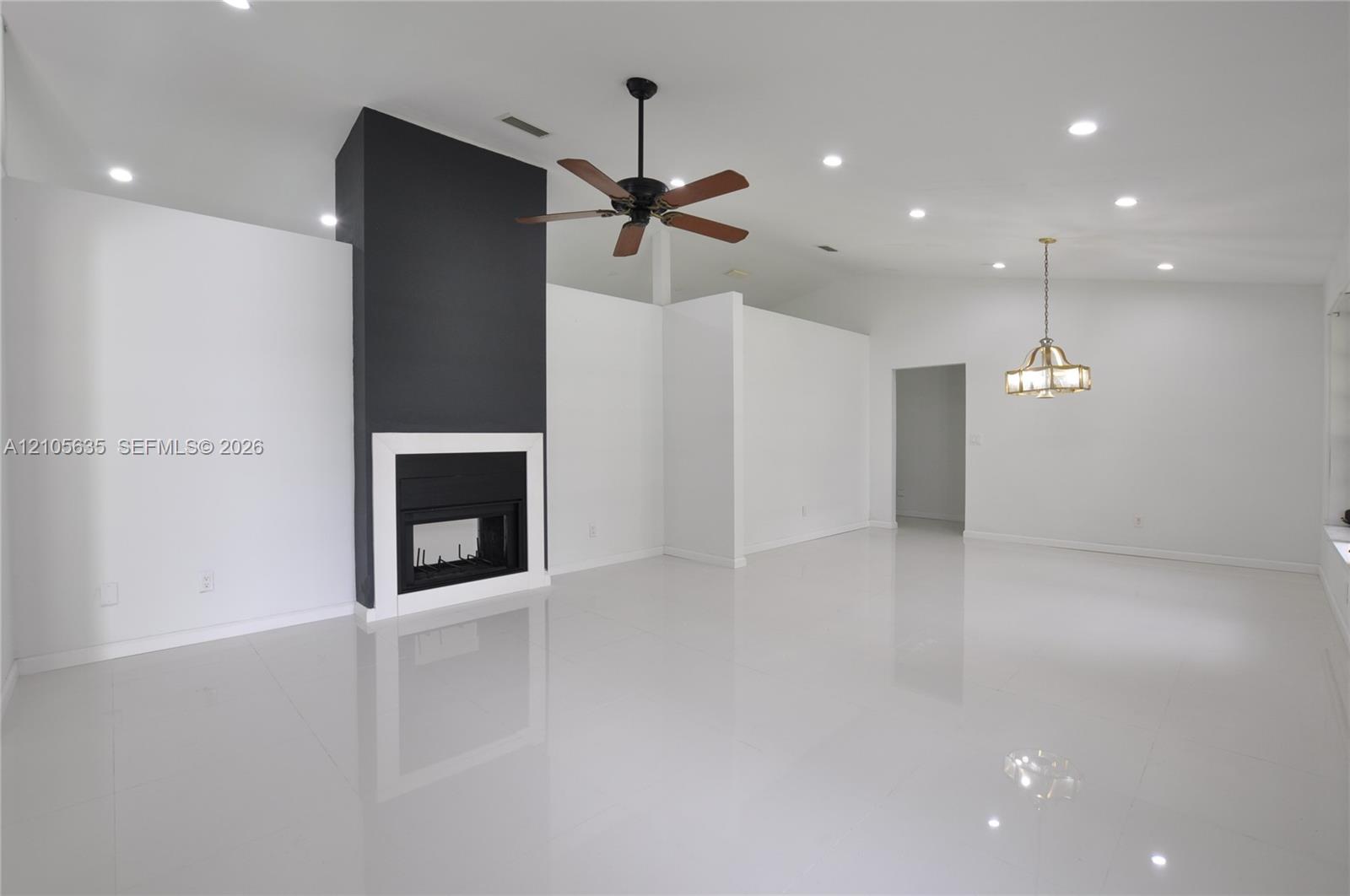 High-gloss tile flooring, vaulted ceilings, focal point fireplace with dark surround, recessed lighting, and multi-arm chandelier