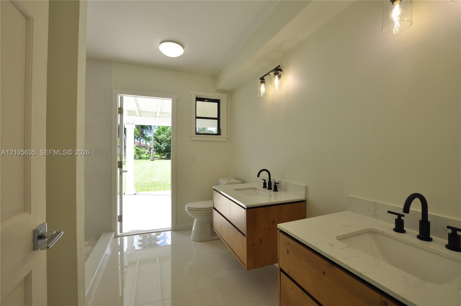 Dual floating vanities featuring light-tone wood-finish cabinetry, white stone-composite countertops, rectangular under-mount sinks, and matte black widespread faucets